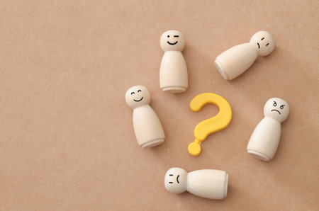 Diverse Wooden Peg Figures with Various Facial Expressions Surrounding a Yellow Question Markの写真素材