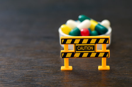 Medication Safety Concept: Yellow Caution Barricade Guarding Colorful Pills and Capsulesの写真素材