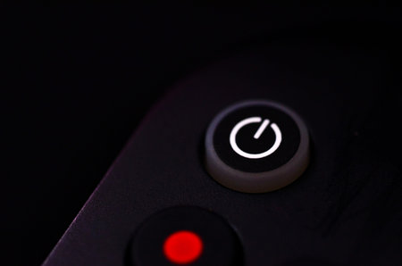 Close up of electronic device power button with glowing white standby symbol on black controller