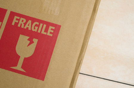 Red Fragile Warning Sticker with Broken Glass Icon on Brown Cardboard Shipping Box
