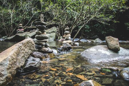Balanced stone pyramide on shore of water fall of mountain lake. Blue mountains in water level...