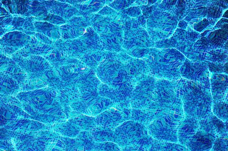 Sun reflection on the blue clear water ripples of swimming pool with mosaic bottom