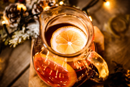 Close up of a piece of lemon in the glass tea pot on a wooden table with christmas lightsの写真素材