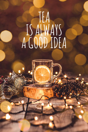 Holiday scene of a glass mug with fruit tea and a piece of lemon in it on a wooden table with bokeh...