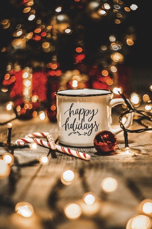 Close up of a white mug with christmas lights and christmas decorations ona wooden table with the message Happy holidaysの写真素材