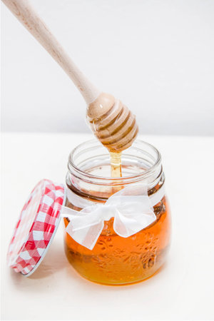 Close up of a honey jar and a honey spoon on a white backgroundの写真素材