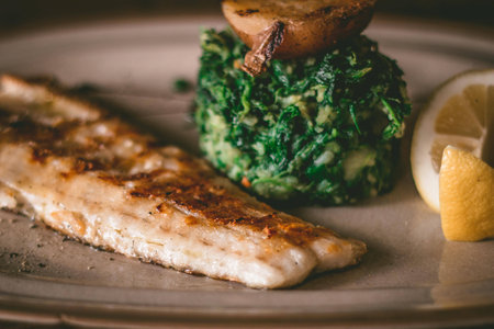 Close up of a delicious grilled fish fillet on a plate with lemon, spinach and potatoes
