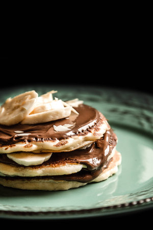 American pancakes with chocolate and banana on a pastel green rustic with black background plate