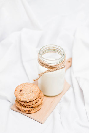 Photo of a jar of milk decorated with rope and cookies on a wooden boardの写真素材