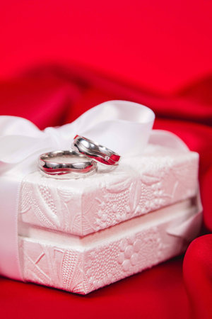 Beautiful close up of wedding rings on white luxury box on red silk backgroundの写真素材