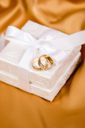 Beautiful photo from above of wedding rings on white luxury box on yellow silk backgroundの写真素材