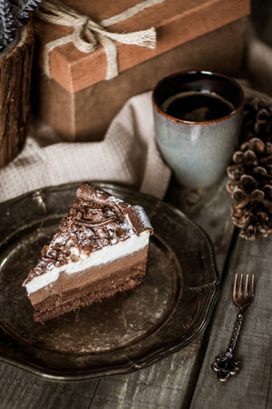 Chocolate birthday cake with flowers, cup of coffee and present box on a wooden tableの写真素材