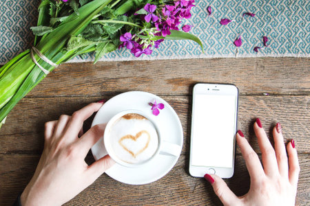 To view of a fresh coffee, spring flowers and a mobile phone template on a wooden tableの写真素材