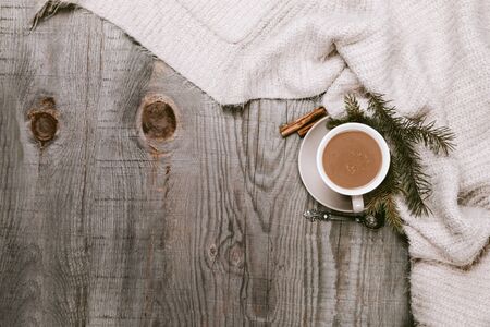 Hot coffee cup wrapped up in a cozy blanket on a wooden tableの写真素材