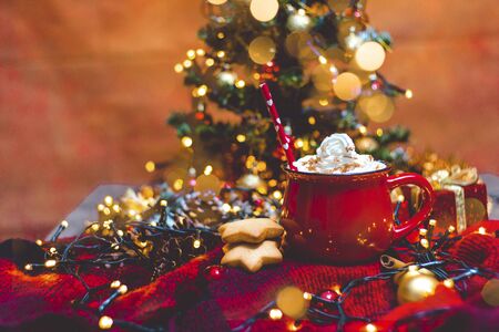 Red mug of hot coffe with Christmas lights, fresh cookies and Christmas treeの写真素材