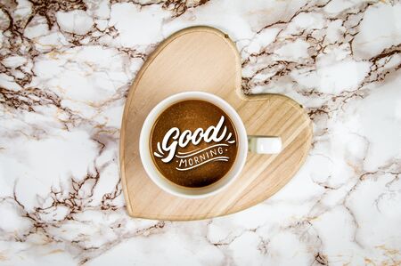 Coffee on a heart shaped holder on a marble background with text Good Morningの写真素材