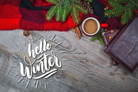 Hot coffee cup wrapped up in a cozy blanket on a wooden table with quote Hello Winterの写真素材