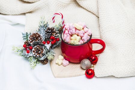 Red mug with marshmallows and winter ornaments on a white sheetsの写真素材