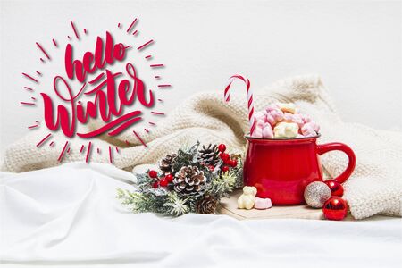 Red mug with marshmallows and winter ornaments on a white sheets with textの写真素材