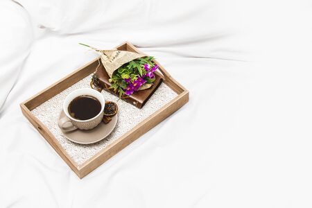 Fresh morning coffee with wrapped flowers on a board on a bed sheet