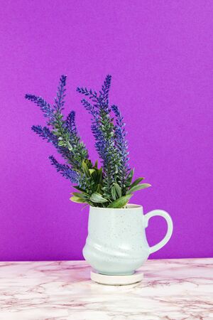 Lavender flowers in a pastel blue mug on a marble table and purple backgroundの写真素材