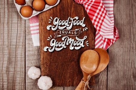 Wooden cutting board on a wooden background with garlic, ladles and eggs with the textの写真素材