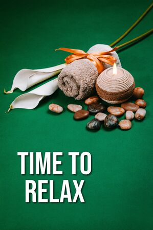 Spa essentials, candle, stones, towel and flowers on a dark green backgroundの写真素材