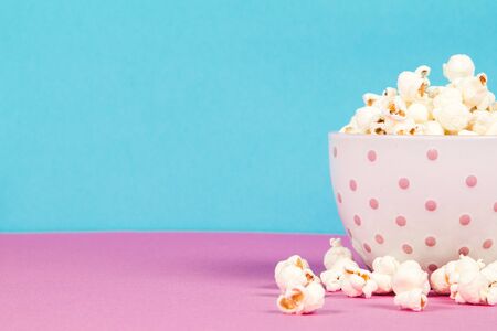 Fresh popcorn in a white pink bowl on pink and blue backgroundの写真素材
