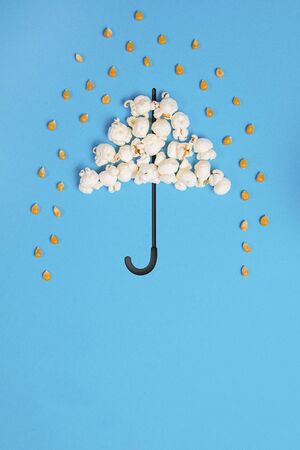 Umbrella and pouring rain drops made out of popcorn on a blue backgroundの写真素材