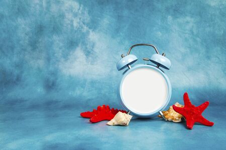 Alarm clock on a blue background with a seashells and starfishの写真素材