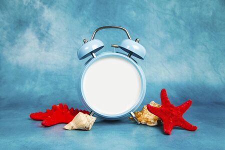 Alarm clock on a blue background with a seashells and starfishの写真素材