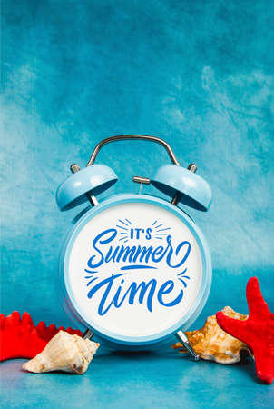 Alarm clock on a blue and yellow background with a seashells and starfishの写真素材