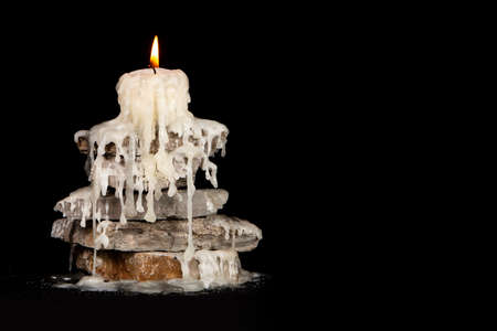 Melted white candle on the rocks on the black backgroundの写真素材