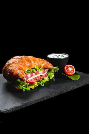 Fresh croissant sandwich with meat and vegetables on black backgroundの写真素材