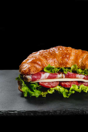 Fresh croissant sandwich with meat and vegetables on black backgroundの写真素材