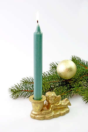 Angle candleholder with green candel, fir branch and golden christmas tree ball on light backgroundの写真素材