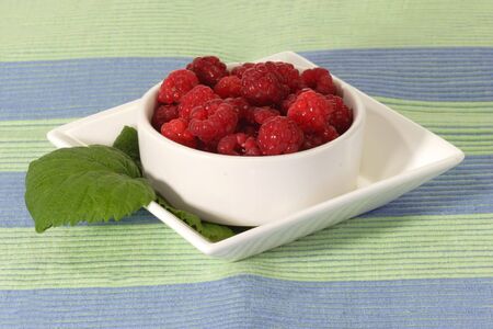 Fresh raspberries with leaves in a white bowl