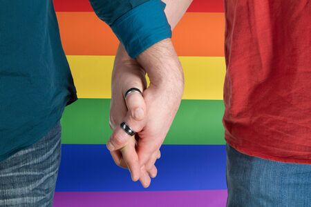 Homosexual couple hands into each other on rainbow flag backgroundの写真素材