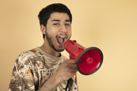 Young Man shouting in speaker on beige backgroundの写真素材