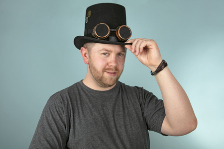 Serious young bearded man in a top hat looking solemnly at the camera over a grey studio backgroundの写真素材