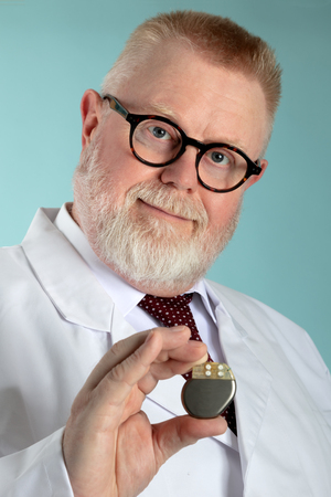 Male Doctor holding Pacemaker in front of camera with blue backgroundの写真素材