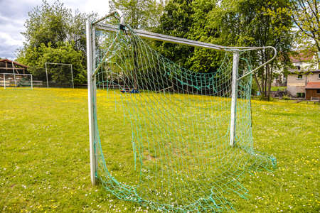 Small empty soccer field with goal and broken net on a beautiful meadowの写真素材