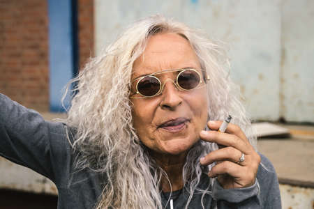 Beautiful woman with long bright curly hair is smoking a cigarette.の写真素材
