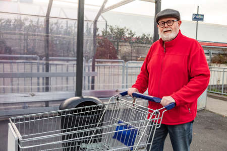 Smiling senior with a cap and red jacket pushing a shopping cartの写真素材