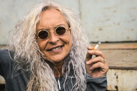 Beautiful woman with long bright curly hair is smoking a cigarette.の写真素材