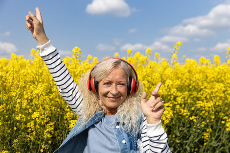 Elderly Woman listen to music with headphones in blooming canola fieldの写真素材