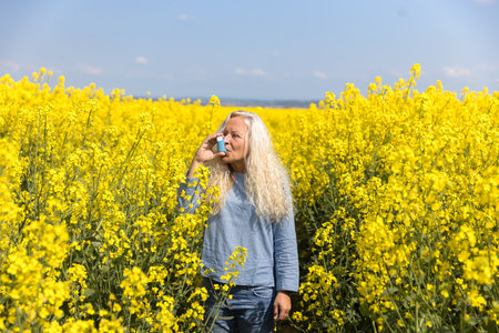 Elderly woman using an asthma metered dose inhaler in a blooming canola fieldの写真素材