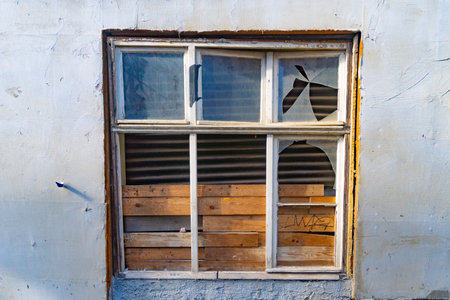 Broken window covered with brown wooden slats as a makeshift solutionの写真素材