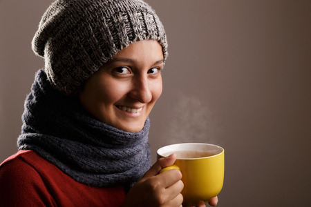 A young woman drinks a cup of hot tea in the winter time isolated on white background.