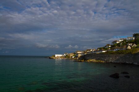 A small fishing village on the coast in Cornwall. A Cornish harbour town on an outcrop of land in a coastal scene. A Cornish landscape or seascape scene at sunset.の写真素材